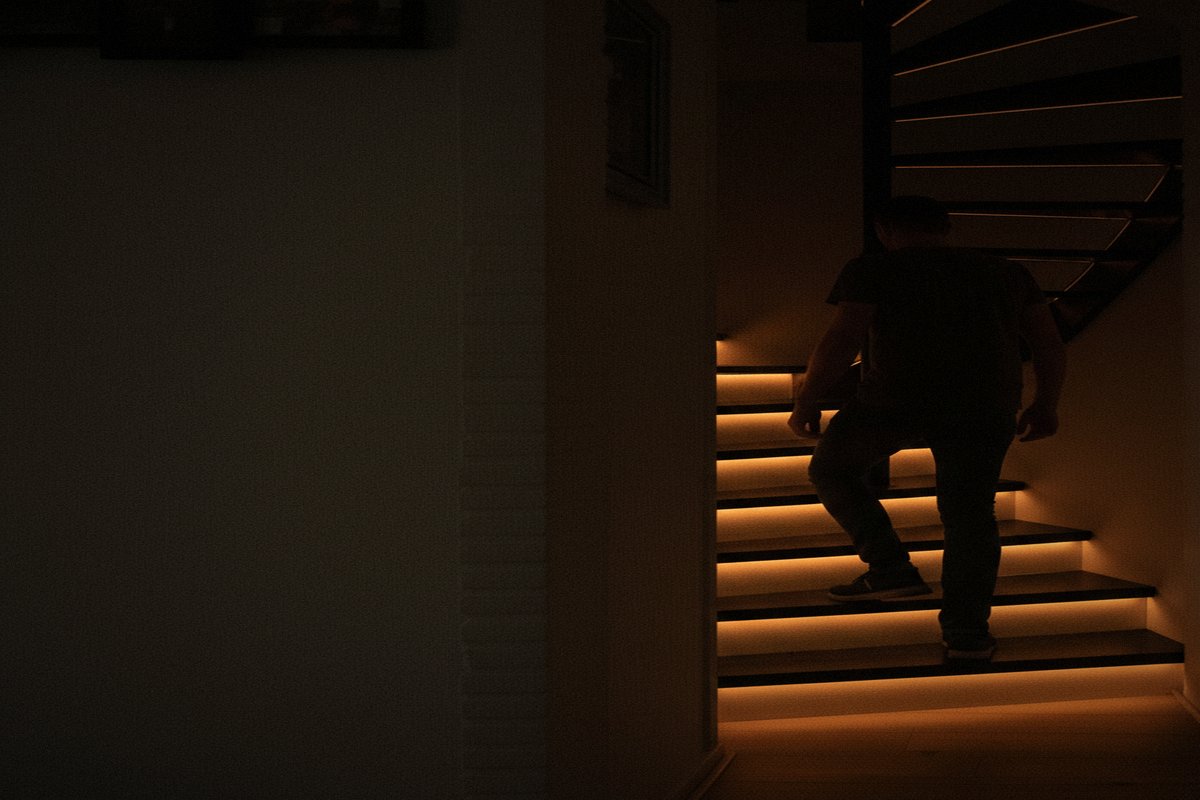 A person climbing the spiral staircase as the amber step lights follow their feet